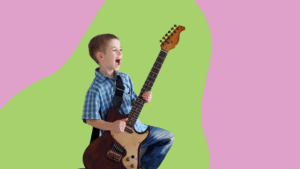 Kuvassa on naurava poika joka soittaa sähkökitaraa.